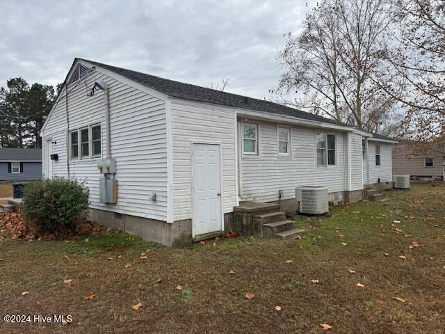 back of property with central AC unit and a yard