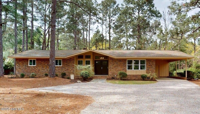 single story home with an attached carport, gravel driveway, and brick siding