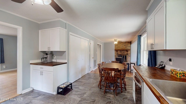 kitchen with ceiling fan, a fireplace, stainless steel dishwasher, ornamental molding, and white cabinetry