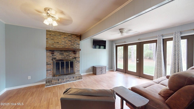 living area featuring ornamental molding, a fireplace, french doors, a ceiling fan, and wood finished floors