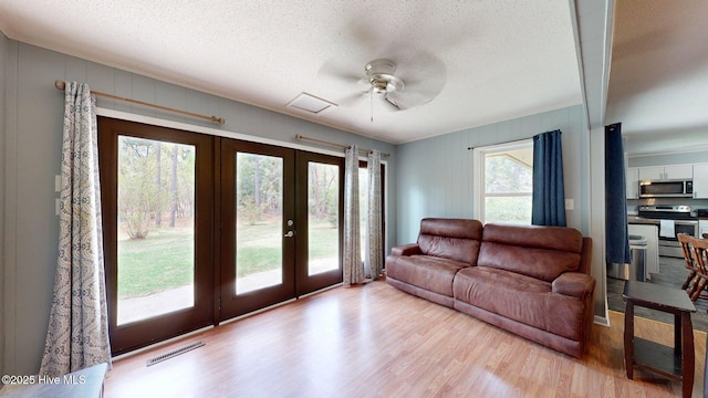 living room with a textured ceiling, a ceiling fan, visible vents, wood finished floors, and french doors