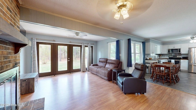 living area with ornamental molding, ceiling fan, light wood-type flooring, a textured ceiling, and french doors