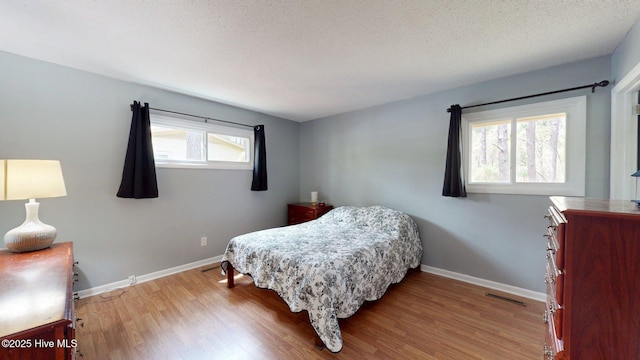 bedroom with visible vents, baseboards, wood finished floors, and a textured ceiling