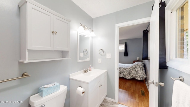 ensuite bathroom with connected bathroom, vanity, toilet, wood finished floors, and baseboards