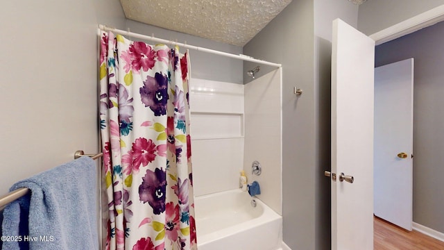 bathroom with a textured ceiling, wood finished floors, shower / bathtub combination with curtain, and baseboards
