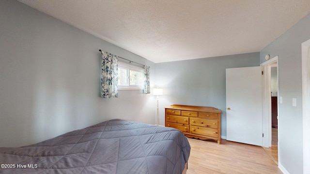 bedroom with light wood-style floors, a textured ceiling, and baseboards
