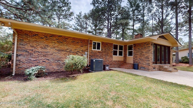 rear view of house featuring central air condition unit, a lawn, entry steps, brick siding, and a chimney