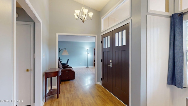 foyer entrance with baseboards, light wood finished floors, high vaulted ceiling, and a chandelier