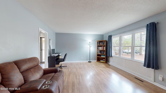interior space with a textured ceiling, wood finished floors, baseboards, and visible vents