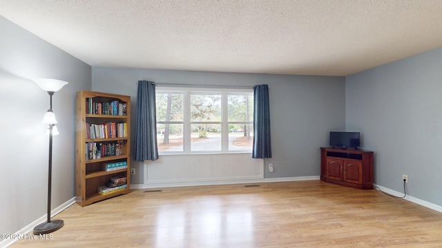 empty room with visible vents, a textured ceiling, and wood finished floors