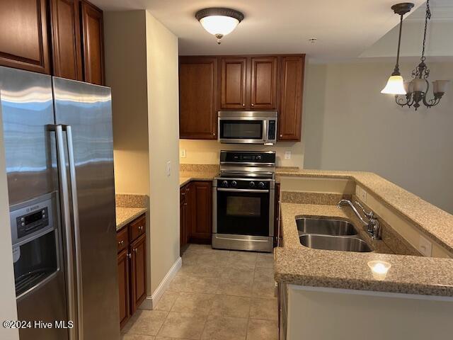 kitchen featuring light stone counters, pendant lighting, stainless steel appliances, a sink, and a peninsula