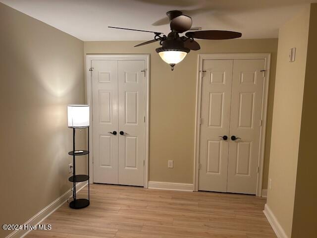 unfurnished bedroom featuring a ceiling fan, light wood-type flooring, baseboards, and two closets