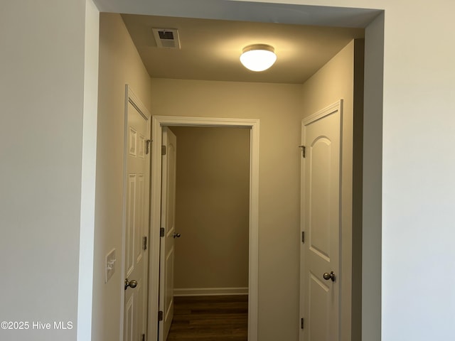 hallway featuring dark wood-type flooring, visible vents, and baseboards