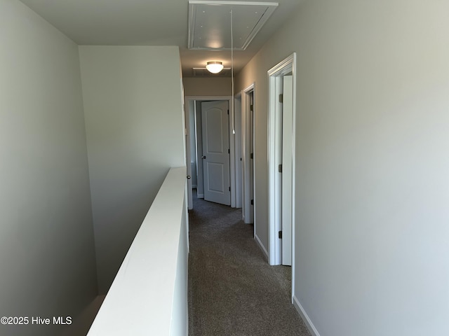 hall featuring attic access, baseboards, and dark colored carpet