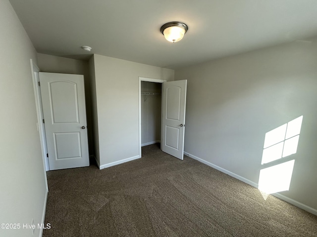 unfurnished bedroom with baseboards, dark carpet, and a closet