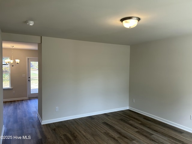 unfurnished room with baseboards, dark wood finished floors, and an inviting chandelier