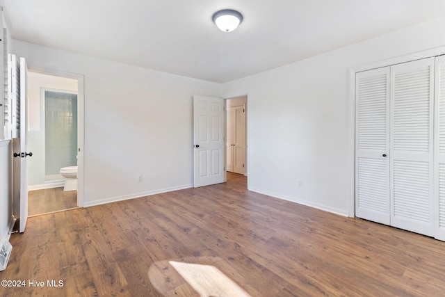 unfurnished bedroom with hardwood / wood-style flooring, ensuite bath, and a closet