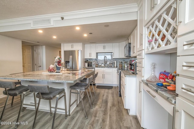 kitchen featuring appliances with stainless steel finishes, a kitchen breakfast bar, wood-type flooring, white cabinets, and a center island