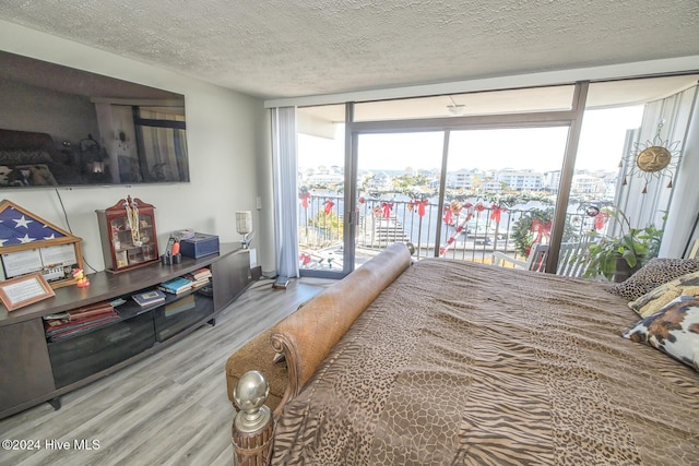 bedroom featuring a textured ceiling, access to exterior, light wood-type flooring, and a wall of windows