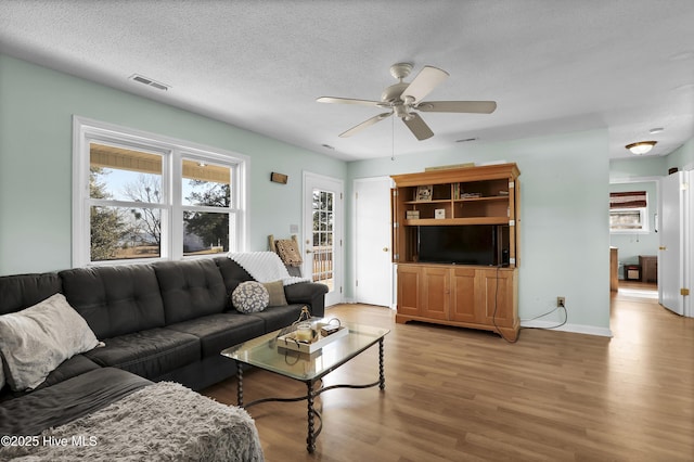 living room with ceiling fan, a textured ceiling, and light wood-type flooring