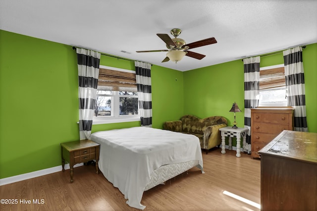 bedroom with ceiling fan, multiple windows, and light hardwood / wood-style flooring