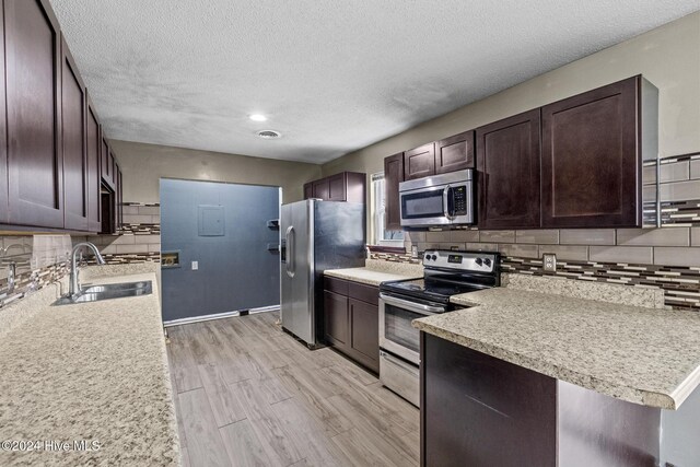 kitchen featuring sink, stainless steel appliances, backsplash, light hardwood / wood-style floors, and a textured ceiling