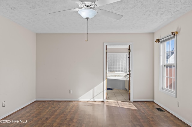 empty room with a textured ceiling, ceiling fan, and dark hardwood / wood-style floors