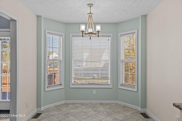 unfurnished room with light tile patterned floors, a textured ceiling, a wealth of natural light, and an inviting chandelier