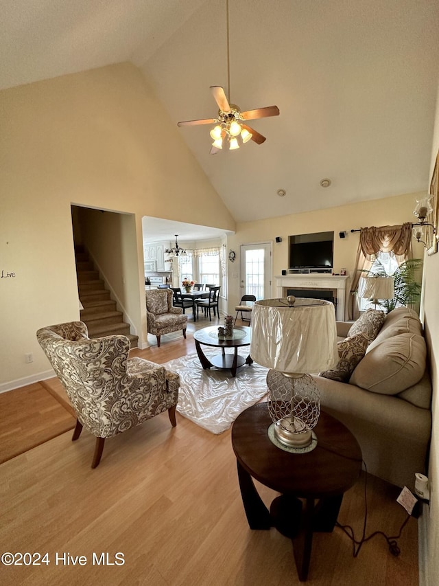 living room with hardwood / wood-style floors, ceiling fan with notable chandelier, and high vaulted ceiling