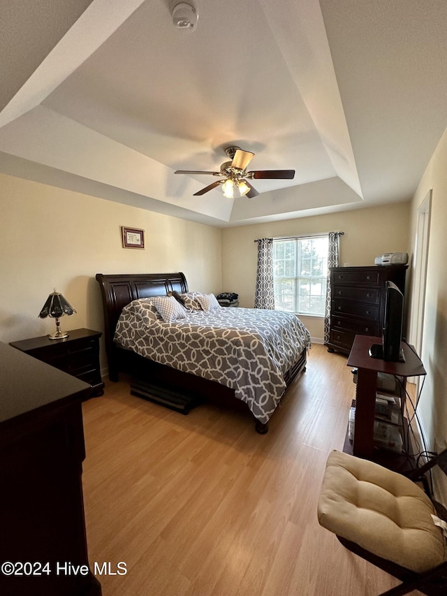 bedroom with light wood-type flooring, a raised ceiling, and ceiling fan