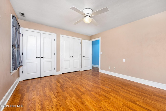 unfurnished bedroom with multiple closets, ceiling fan, and hardwood / wood-style floors