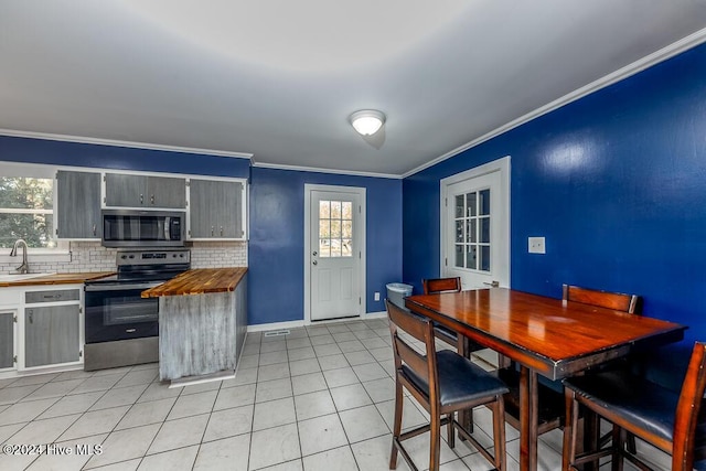 kitchen with wooden counters, crown molding, decorative backsplash, light tile patterned flooring, and stainless steel appliances