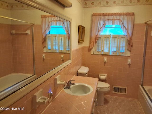 full bathroom with tile patterned floors, combined bath / shower with glass door, toilet, vanity, and tile walls