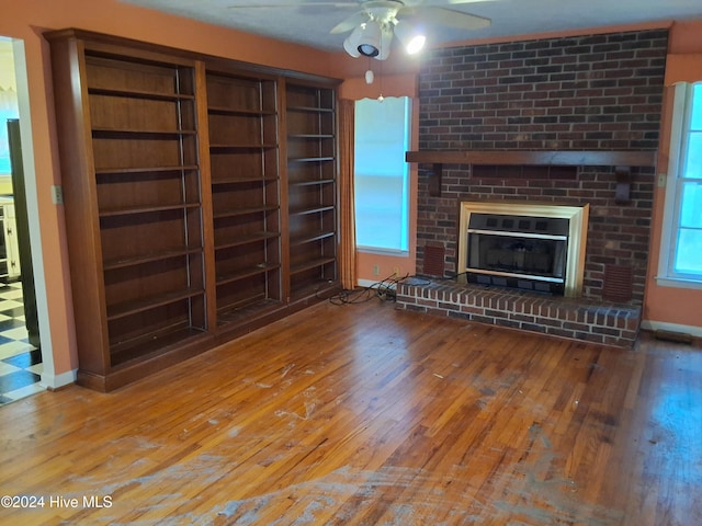 unfurnished living room featuring hardwood / wood-style floors, ceiling fan, and a brick fireplace