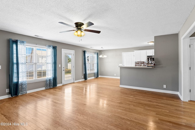 unfurnished living room featuring light hardwood / wood-style flooring, ceiling fan with notable chandelier, and a textured ceiling