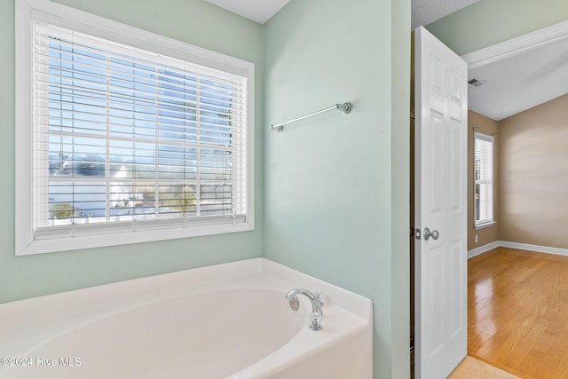 bathroom with hardwood / wood-style floors, a textured ceiling, a tub to relax in, and a wealth of natural light