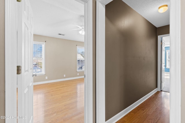 hallway with a textured ceiling and light hardwood / wood-style flooring