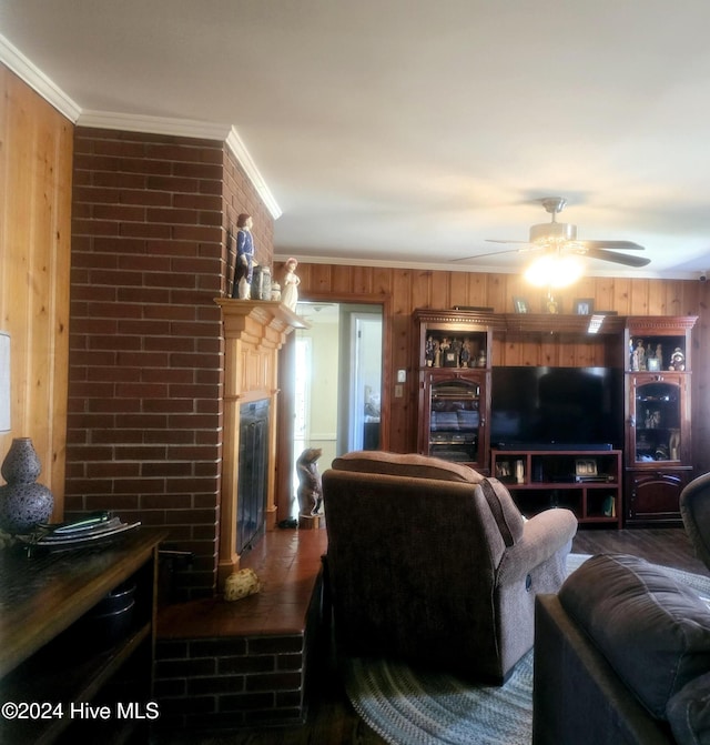 living room with ceiling fan, a brick fireplace, dark hardwood / wood-style flooring, crown molding, and wood walls