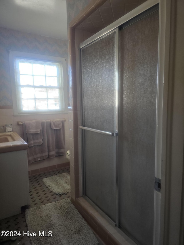 bathroom featuring a shower with door, vanity, tile walls, and toilet