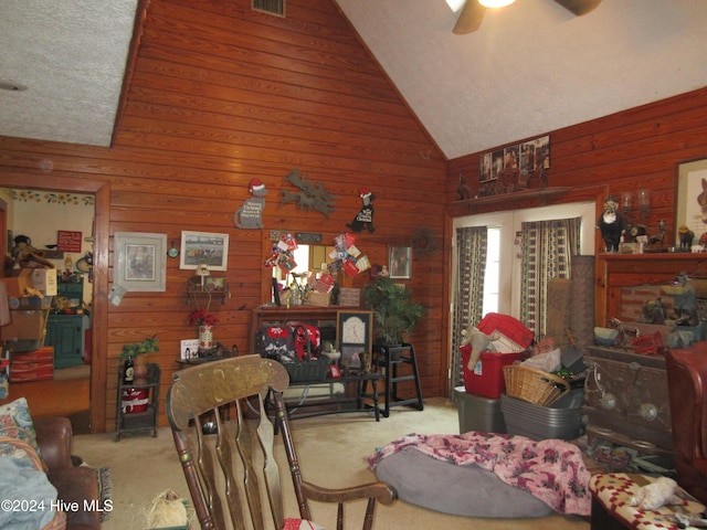 carpeted dining room with ceiling fan, wood walls, and high vaulted ceiling