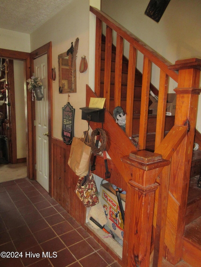 stairway with tile patterned flooring, a textured ceiling, and wood walls