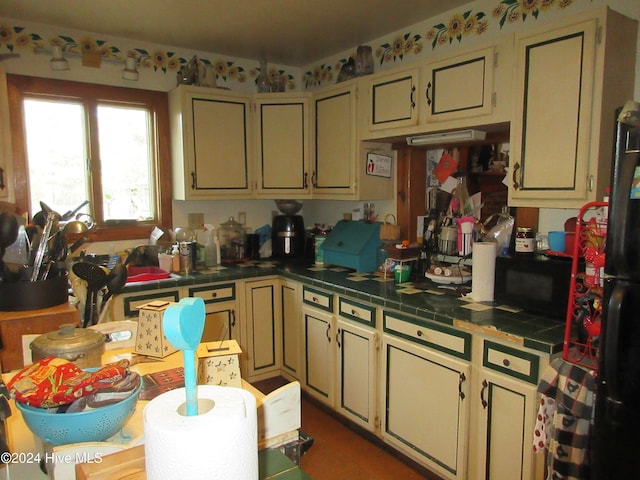 kitchen featuring tile counters, black appliances, and cream cabinetry