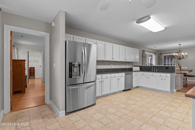 kitchen with sink, stainless steel fridge with ice dispenser, pendant lighting, white cabinets, and ceiling fan with notable chandelier