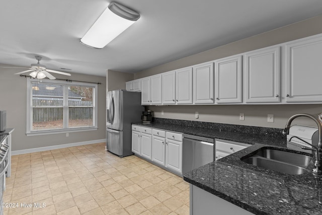 kitchen featuring dark stone counters, stainless steel appliances, ceiling fan, sink, and white cabinets