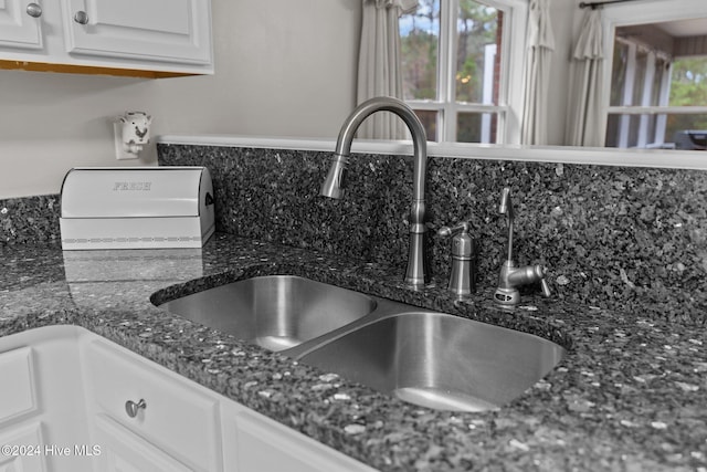 room details featuring white cabinets, backsplash, dark stone countertops, and sink