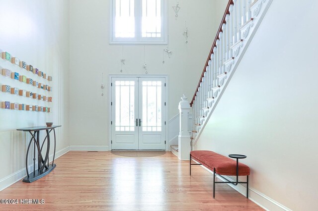 foyer entrance featuring plenty of natural light, a towering ceiling, french doors, and light wood-type flooring