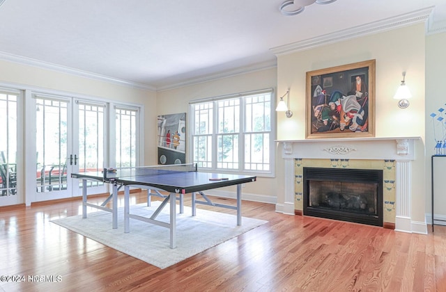 game room featuring a tiled fireplace, ornamental molding, and light hardwood / wood-style flooring