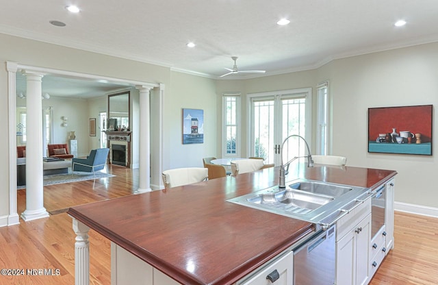 kitchen featuring light wood-type flooring, ornamental molding, ceiling fan, a center island with sink, and white cabinetry