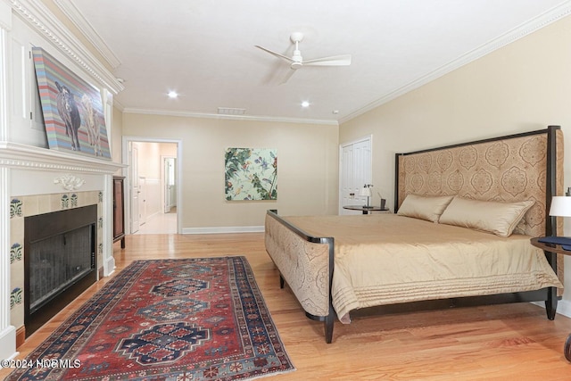 bedroom featuring a tile fireplace, ceiling fan, crown molding, light hardwood / wood-style floors, and a closet