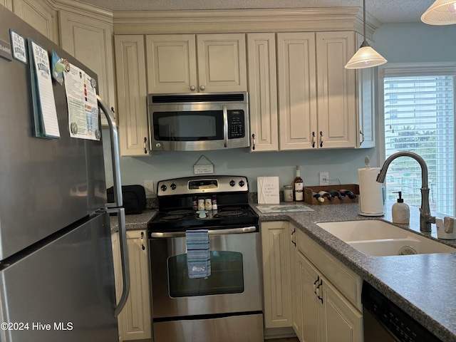 kitchen featuring cream cabinetry, appliances with stainless steel finishes, decorative light fixtures, and sink